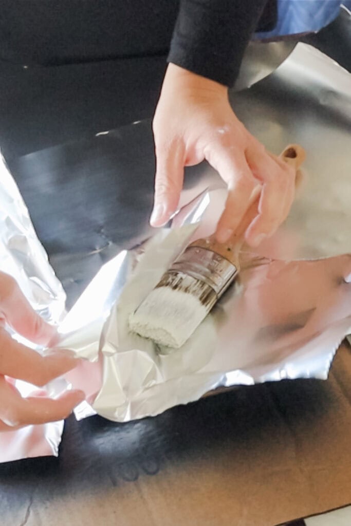 Hands wrapping a paintbrush with aluminum foil