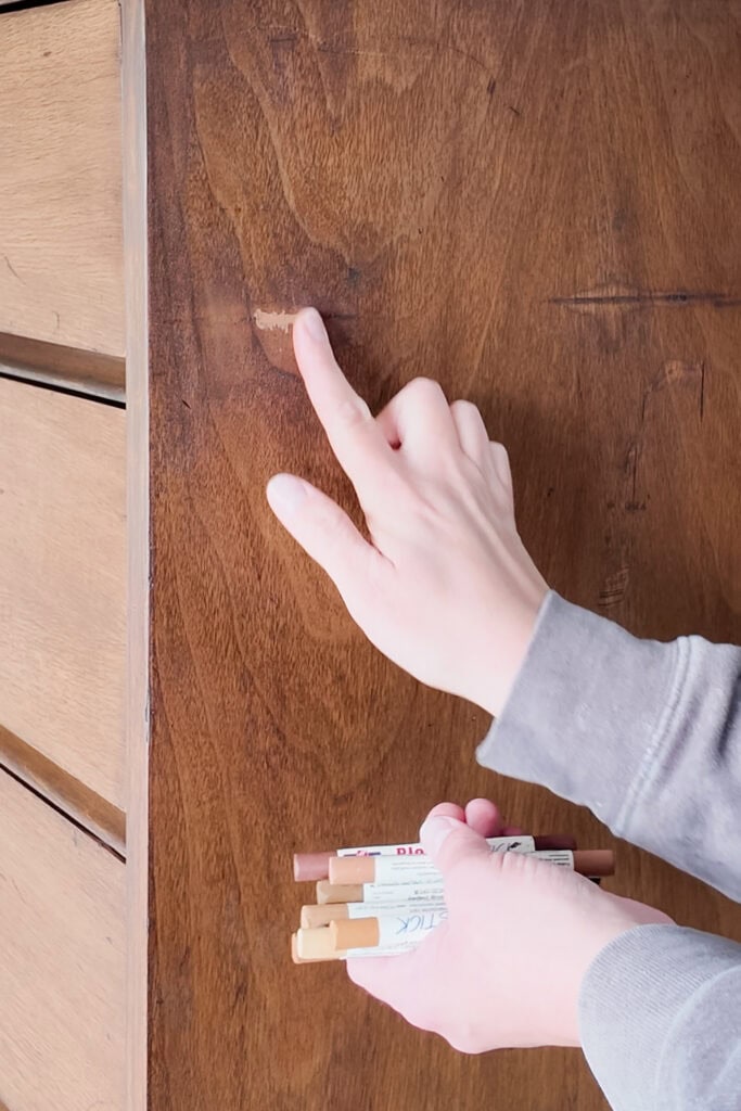 A person blends wood repair marker on wood, holding other markers in their other hand.