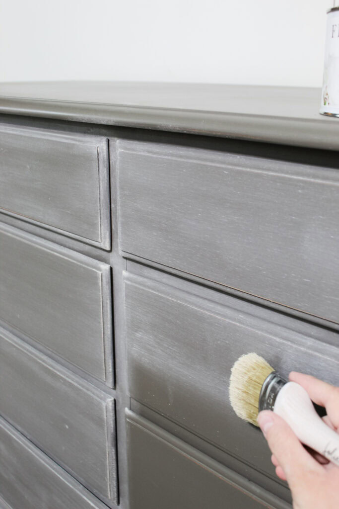 Hand applying wax with a brush to a gray dresser