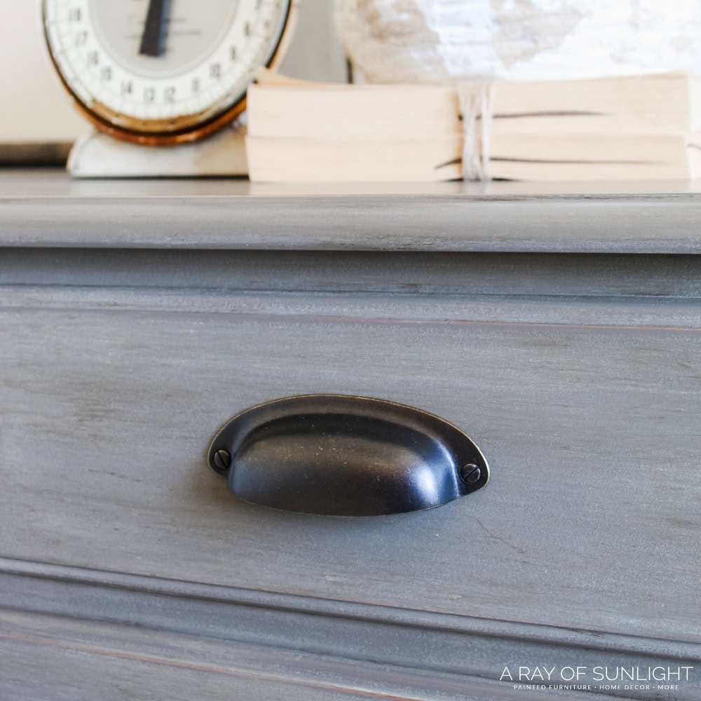 Close up of a dark cup pull on a gray wooden drawer