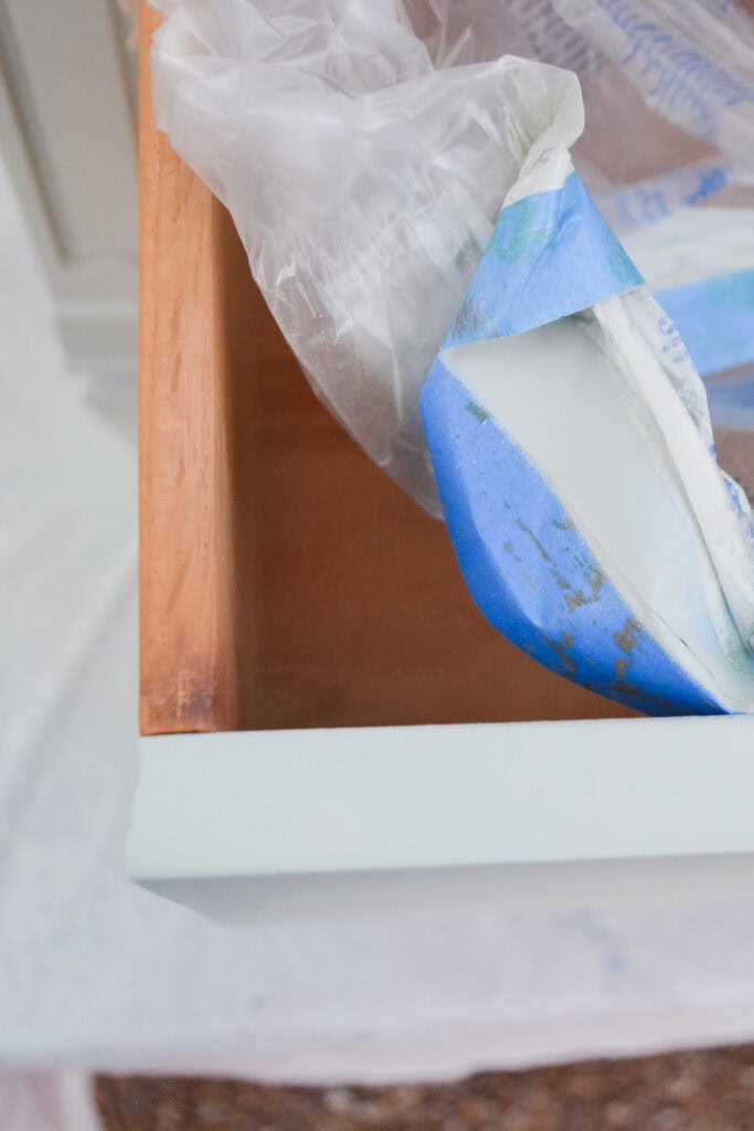 A closeup of a wooden drawer with painters tape and plastic covering over it