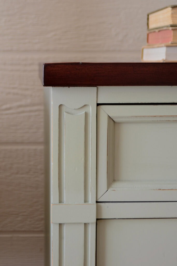 Closeup of a light green dresser with a dark wooden top