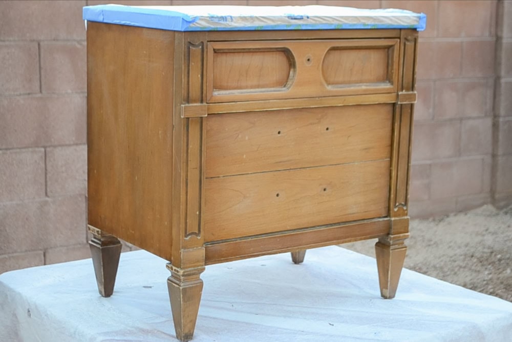 A wooden dresser on table outdoors, covered with plastic and tape on the top.