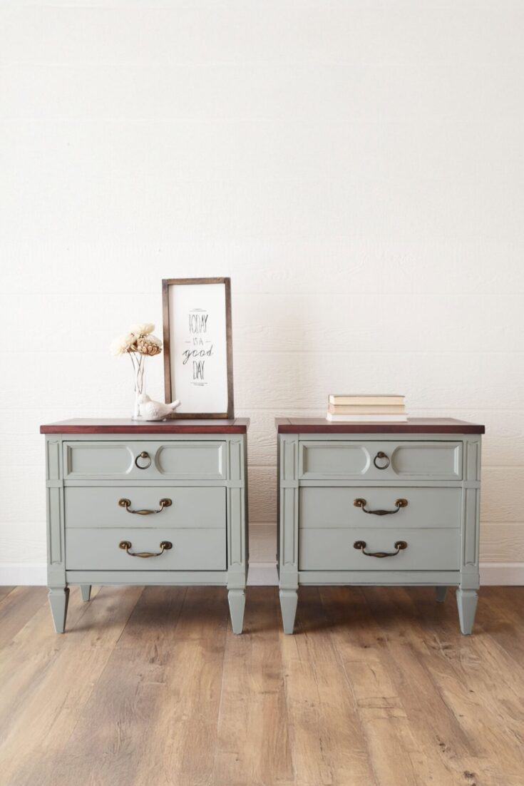 Two light gray nightstands with dark wood tops, decor, and books, on a wooden floor against a white wall.