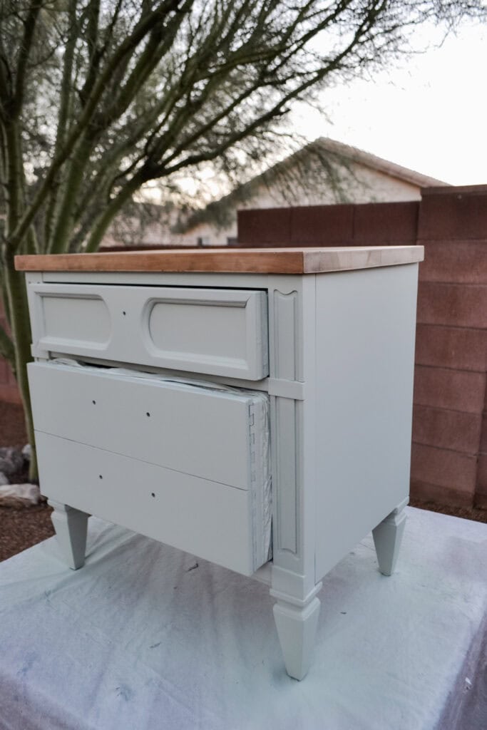 A light green dresser with two slightly open drawers placed outdoors