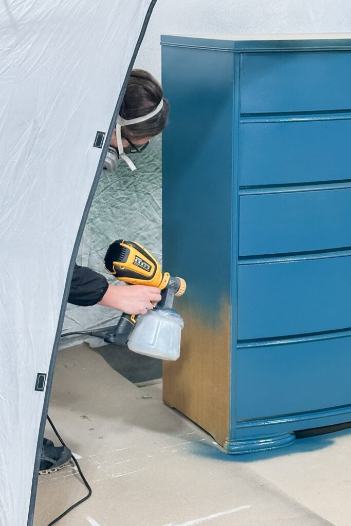 Person spray painting the side of wooden dresser