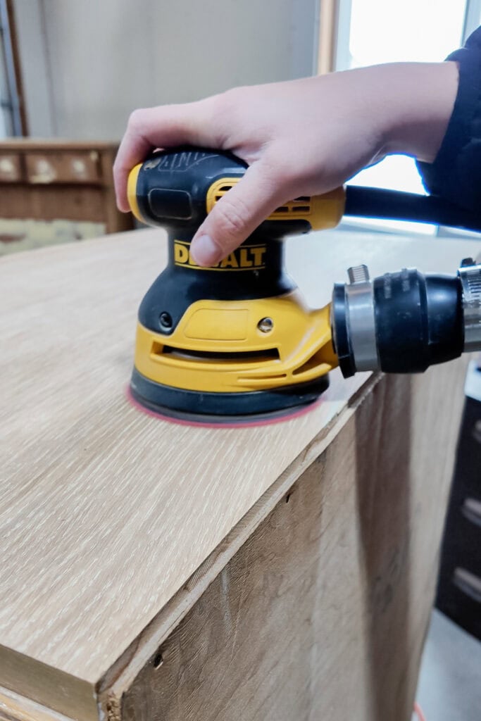 Hand using a yellow orbital sander on a wooden surface.