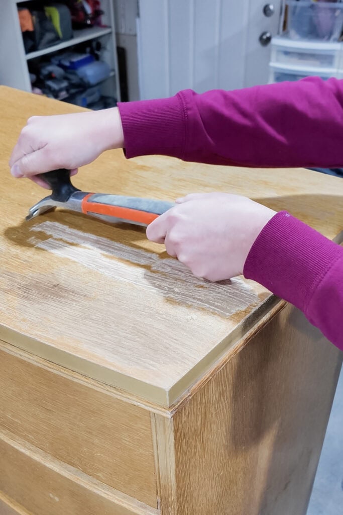 Person using a tool to scrape the surface of a wooden dresser