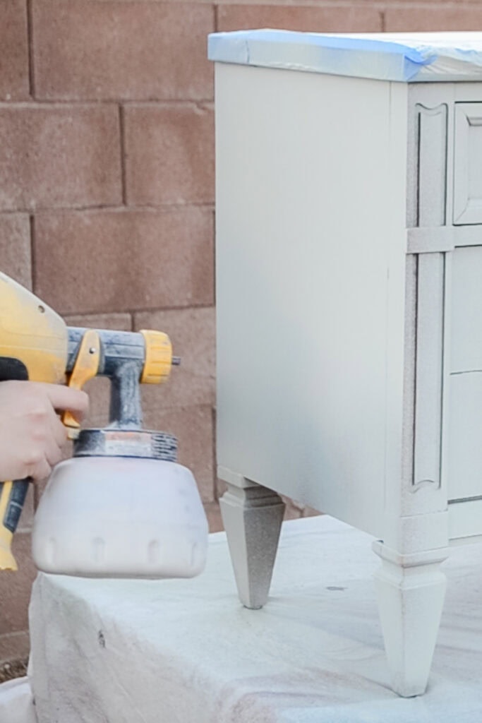 Person using a paint sprayer to apply green paint on dresser