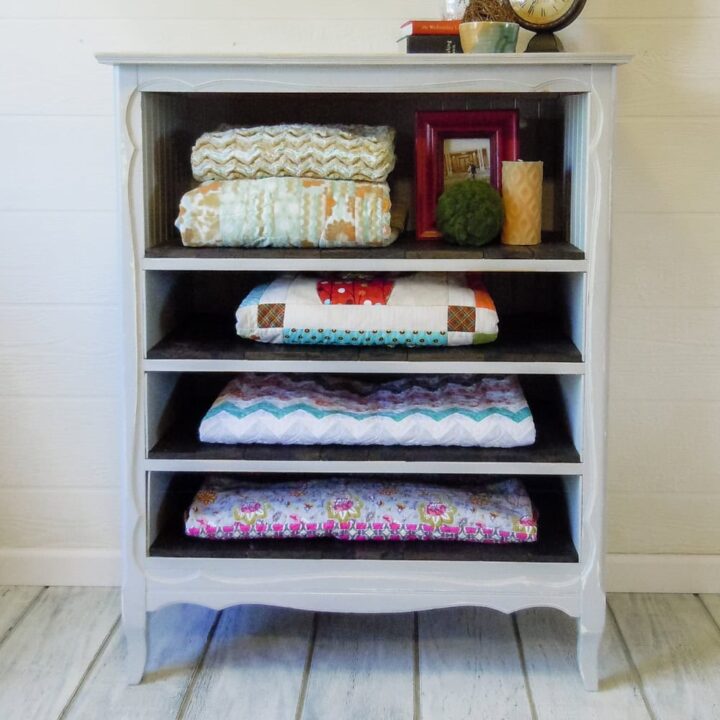 A white wooden shelf holds four folded quilts