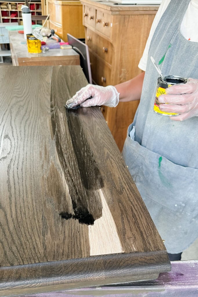 Person applying dark wood stain to a wooden surface