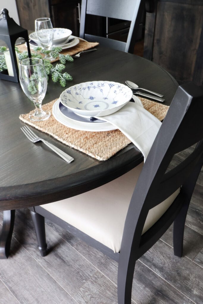 Table setting with a bowl, plate, glass, silverware, and napkin on a woven placemat at a dark wooden table.