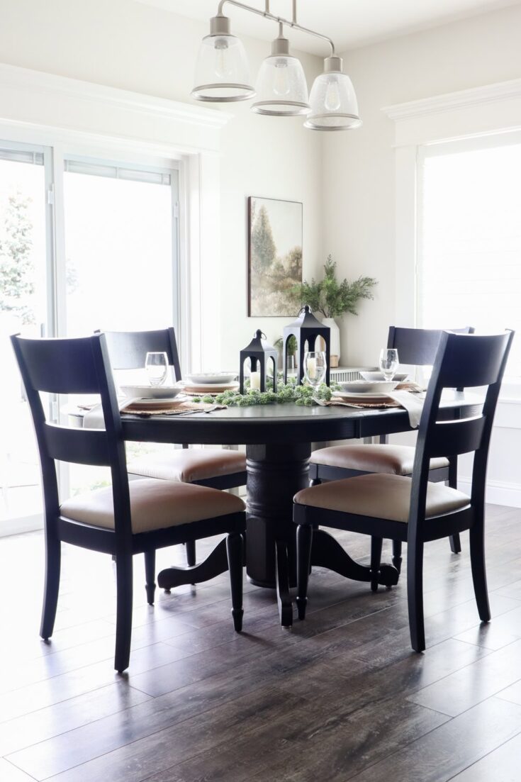 A round dining table with four dark chairs set for a meal in a bright, modern dining room.