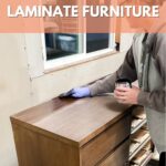 Person staining a wooden dresser next to a window