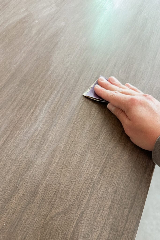 Hand sanding a wooden surface with a small piece of sandpaper.