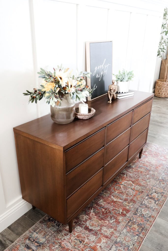 Refinished dresser with decorative items, flowers, and framed art on top