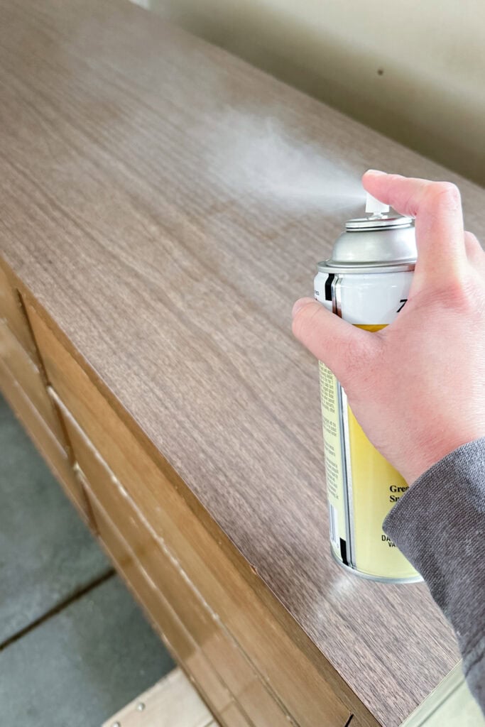 Hand spraying clear shellac from a can onto a laminate surface.