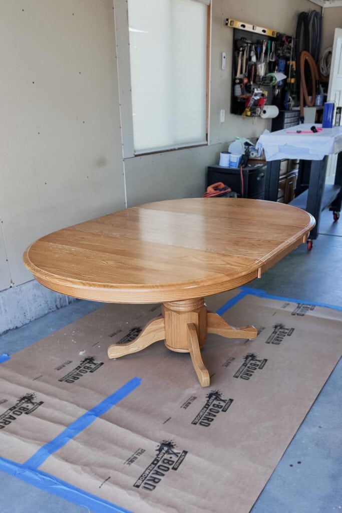 An oval wooden table on cardboard in a garage