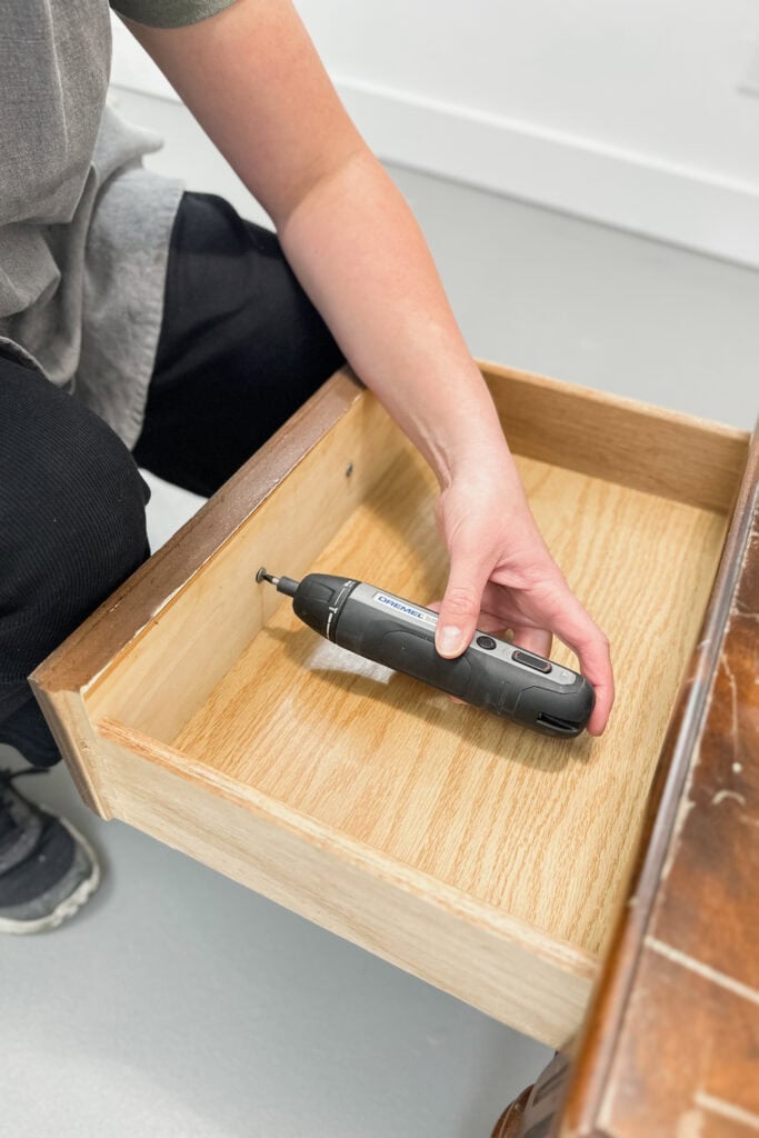 Person holding a power tool inside an empty wooden drawer, preparing for a repair or installation.