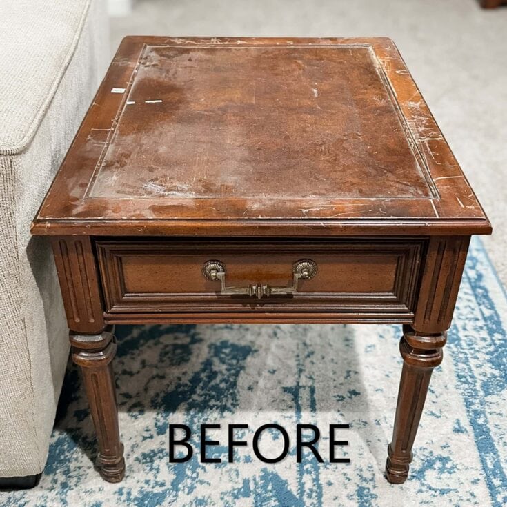 A scratched, worn wooden end table with a drawer, labeled “BEFORE,” next to a beige sofa on a blue rug.