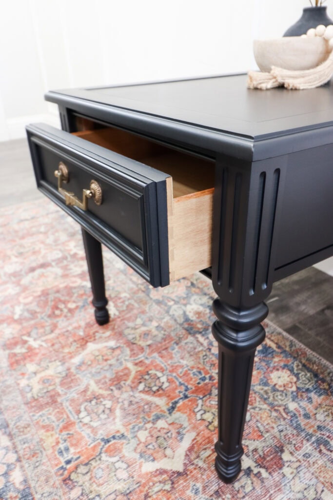 Black wooden side table with an open drawer, placed on a colorful patterned rug.