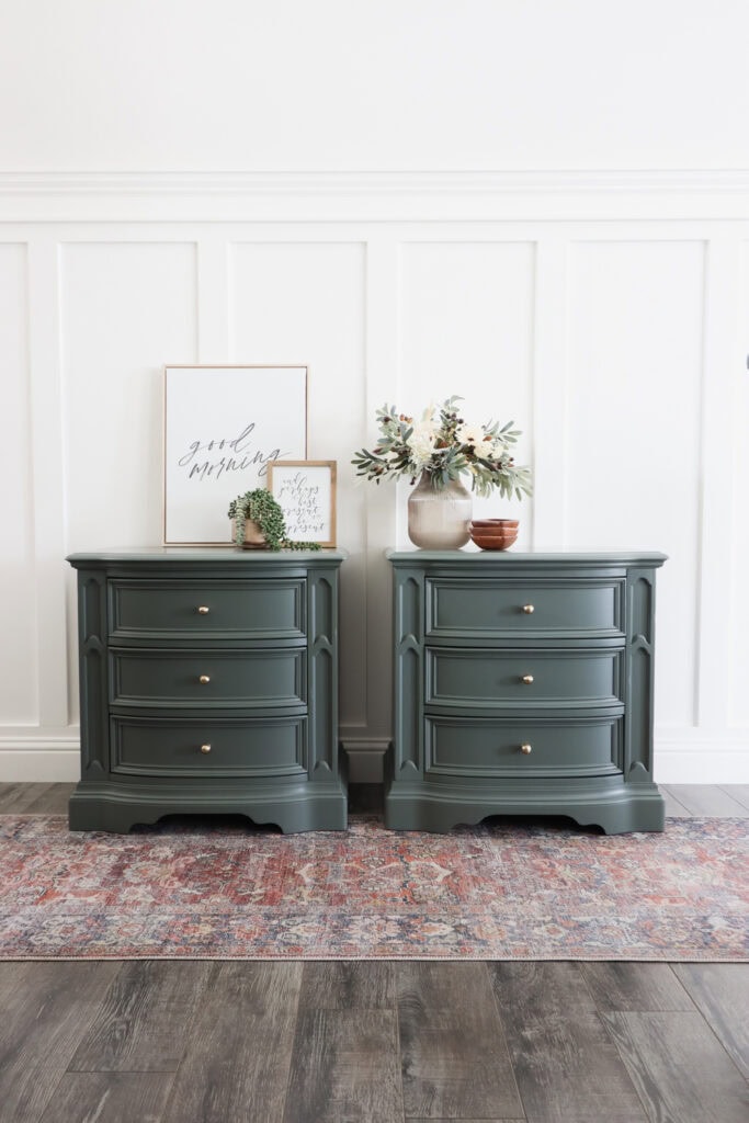 Two green dressers with decor, framed art, and vases, against a white paneled wall on a patterned rug.