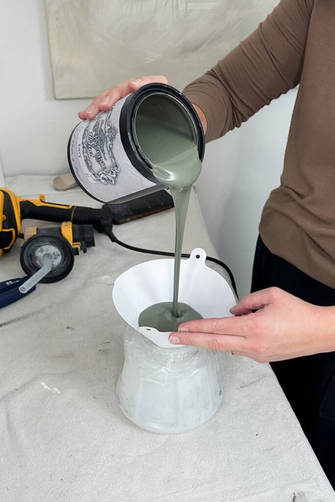 Person pouring green paint from a can through a filter into a sprayer container
