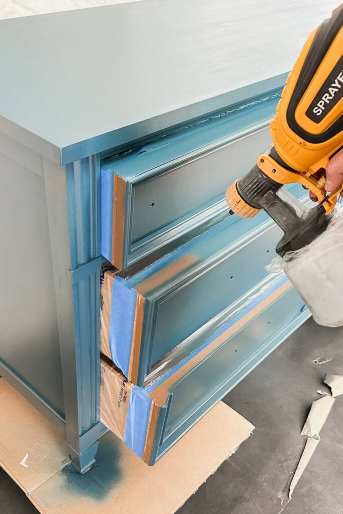 A person spray paints drawers partially open and taped.