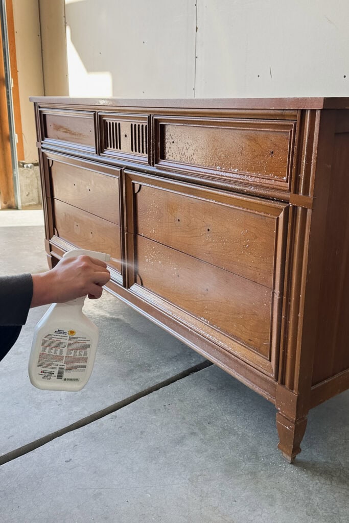 Hand spraying cleaner on a wooden dresser in a garage