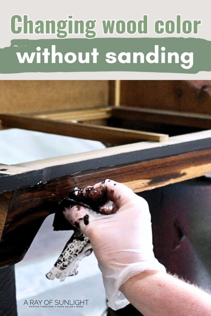 Hand wearing glove applies wood stain to bottom of wood furniture