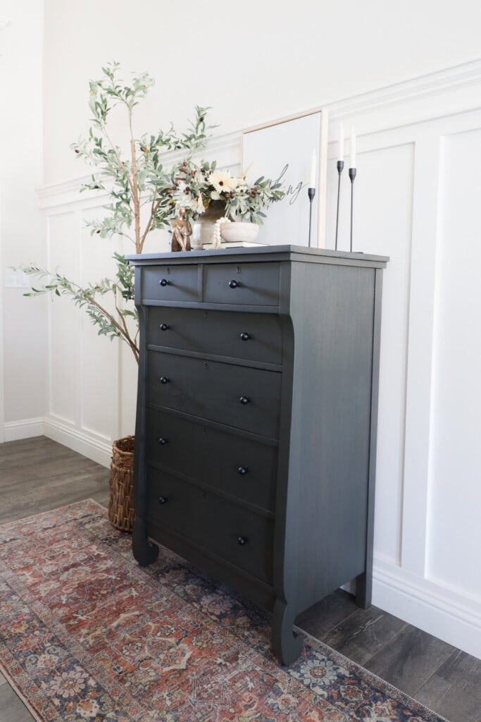 Tall dark dresser with decor on top and plant beside it