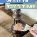 A hand in a glove uses a brush to apply chemical stripper to dark stained wood furniture. Text reads: Removing wood stain.