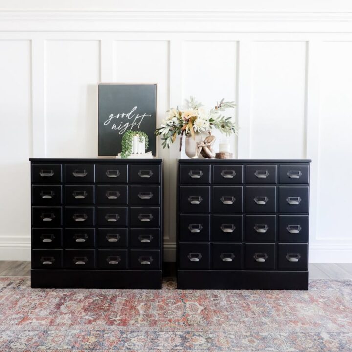 Two black drawer cabinets with a floral arrangement, books, and framed art displayed on top against a white wall.