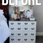 A white dresser with dark handles beside a bed.