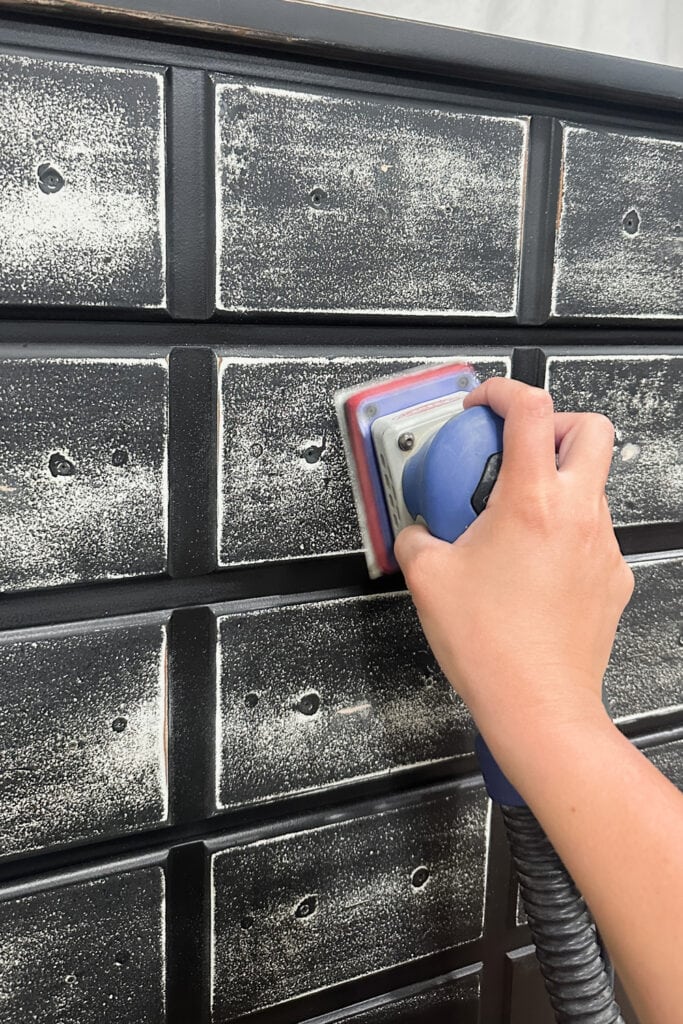 A hand uses an electric sander to sand drawer fronts