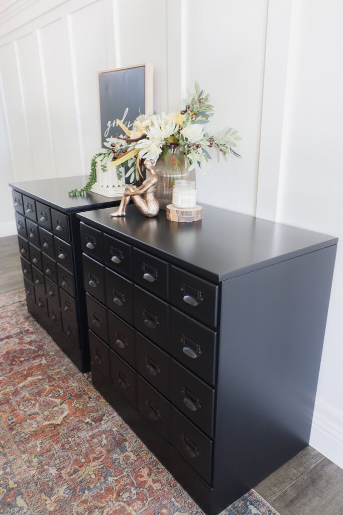 Black cabinets with drawer pulls, decorated with a vase of flowers, books, and a gold figurine on top.