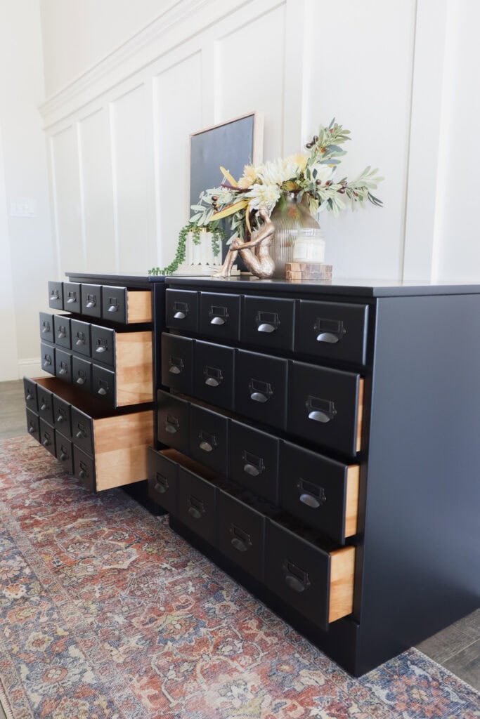 Black card catalog nightstands with open drawers, decorative items, and a vase of flowers on top.