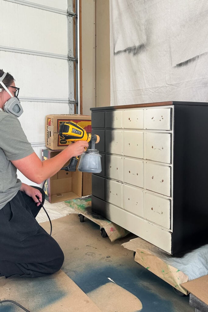 Natalie wearing a respirator while spray painting a white nightstand black