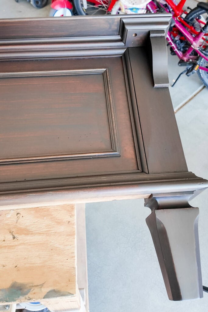 A dark wood footboard with decorative trim placed on a workbench in a garage.
