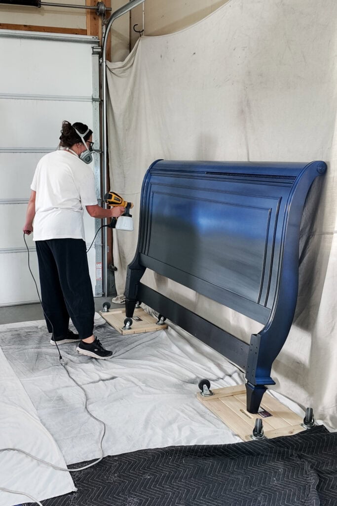 Person wearing respirator sprays topcoat on a dark wooden headboard