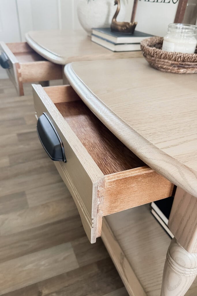Two wooden drawers are partially open on a light wood table with black handles