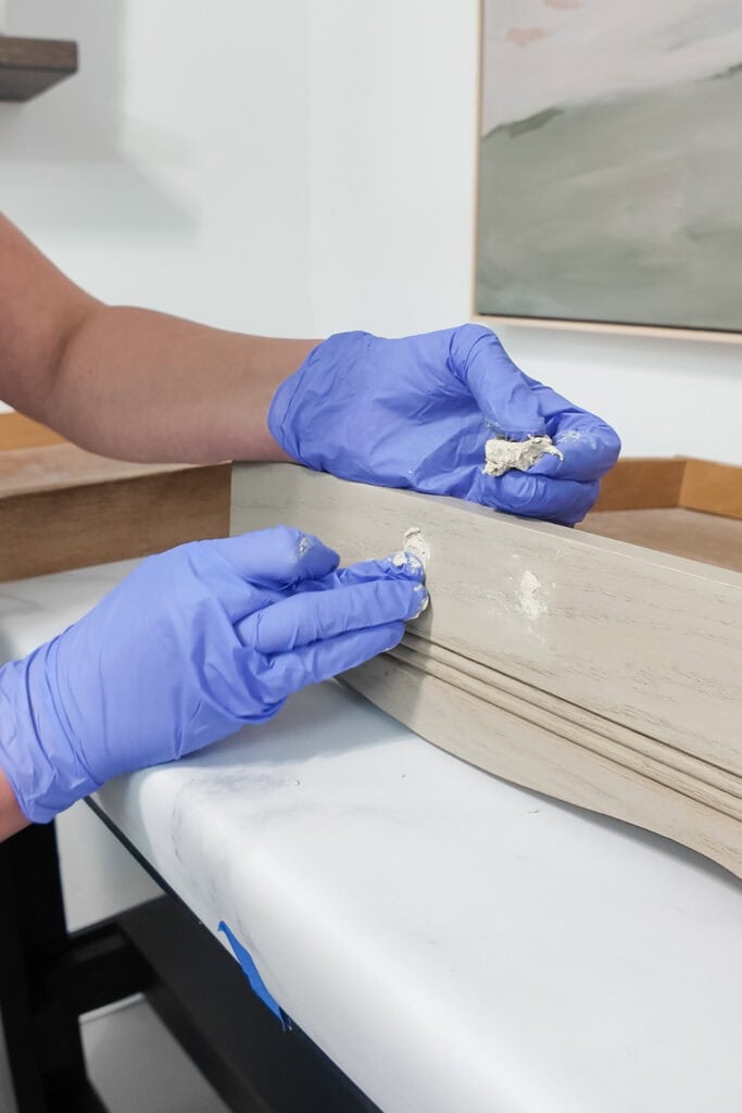 Person in blue gloves applying wood filler to drawer holes