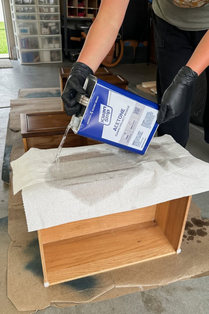 Person pours acetone from a metal can onto a paper towel covered wooden drawer