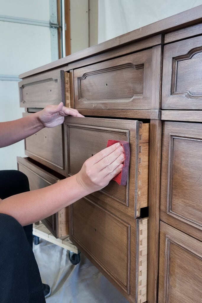 A person sanding a wooden dresser drawer with foam pad