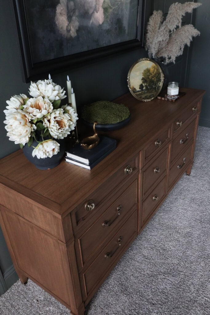 Wood sideboard with drawers, white flowers, candles, and art decor placed on top.
