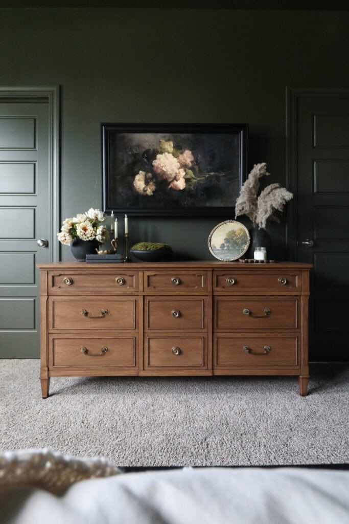 Wooden dresser with nine drawers, floral decor, framed art, and two doors in the background.