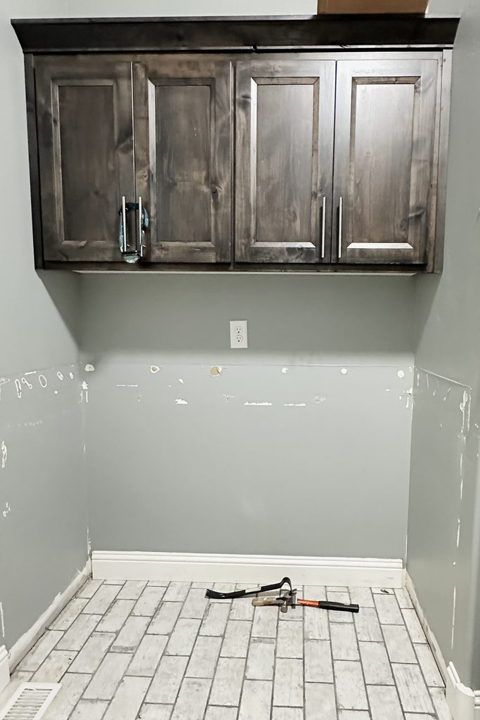 Dark wooden cabinets on a gray wall above a partially finished space with tools on a tiled floor.