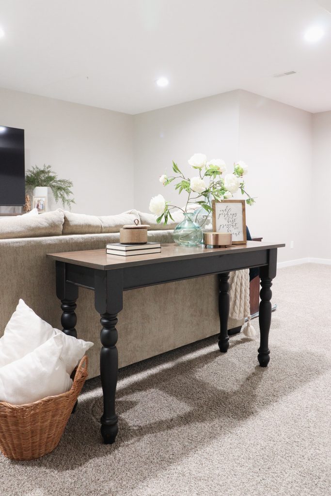 A black console table behind a beige sofa holds books, candles, and a vase of white flowers.