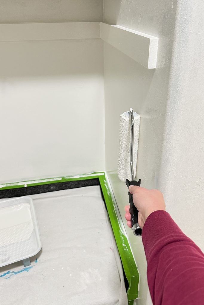 A person uses a paint roller to paint wall white