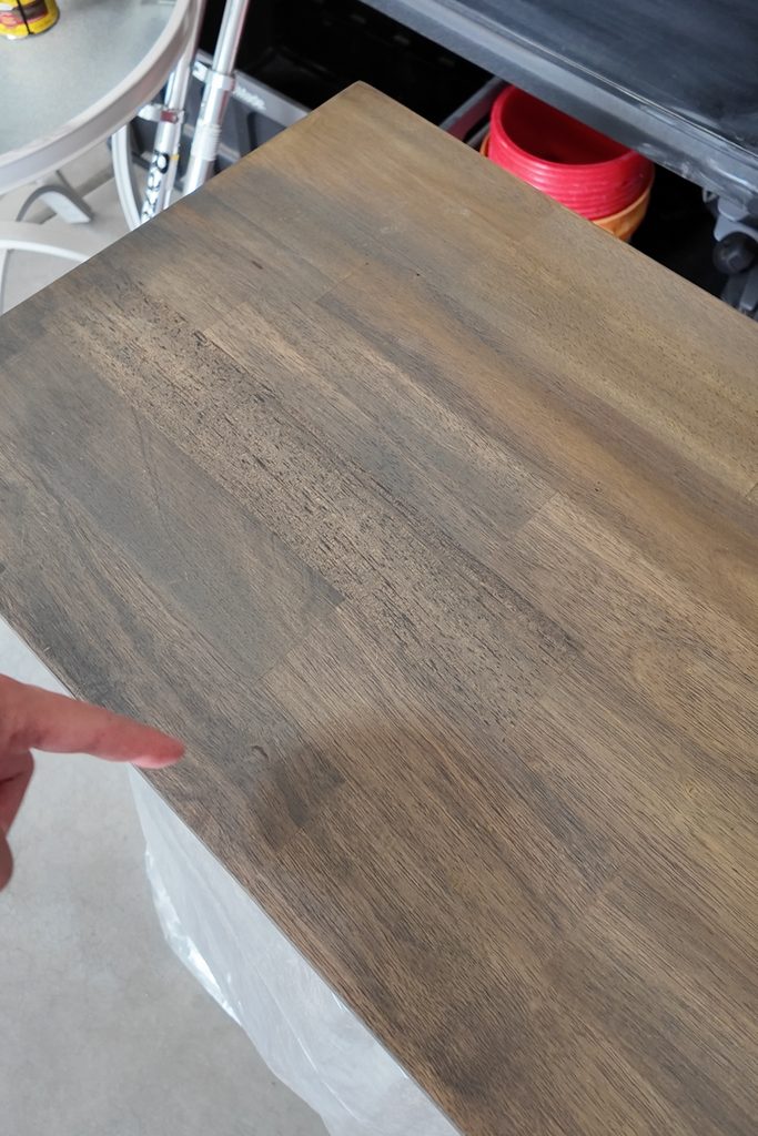 A finger points at splotchy stain on a wooden tabletop